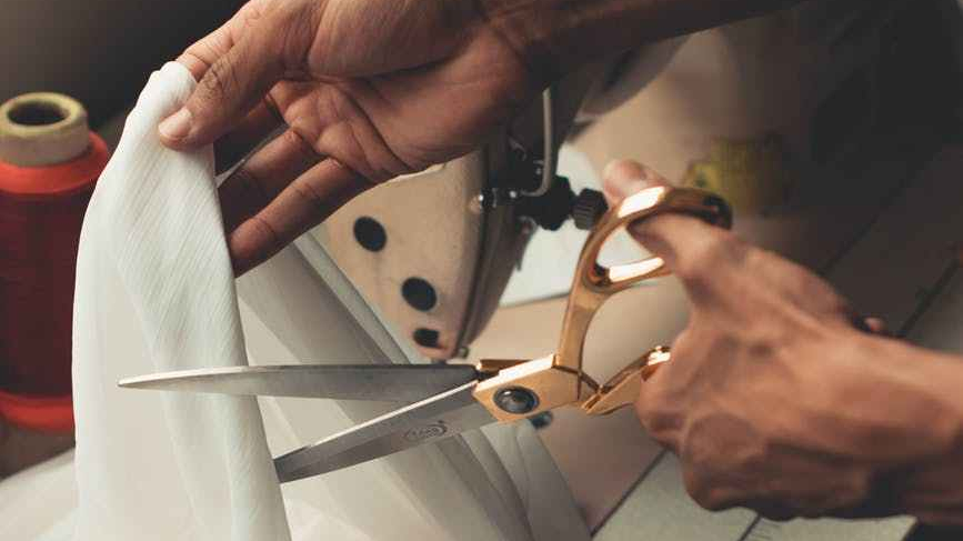 free image, hands using scissors on fabric with a sewing machine in the background